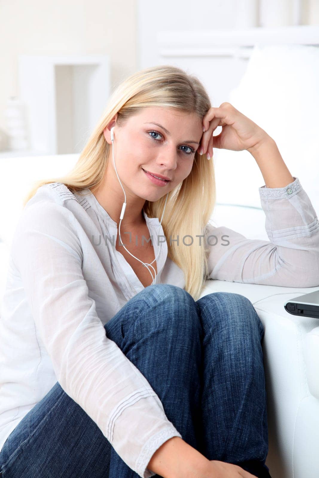 Beautiful blond woman with headphones sitting on sofa