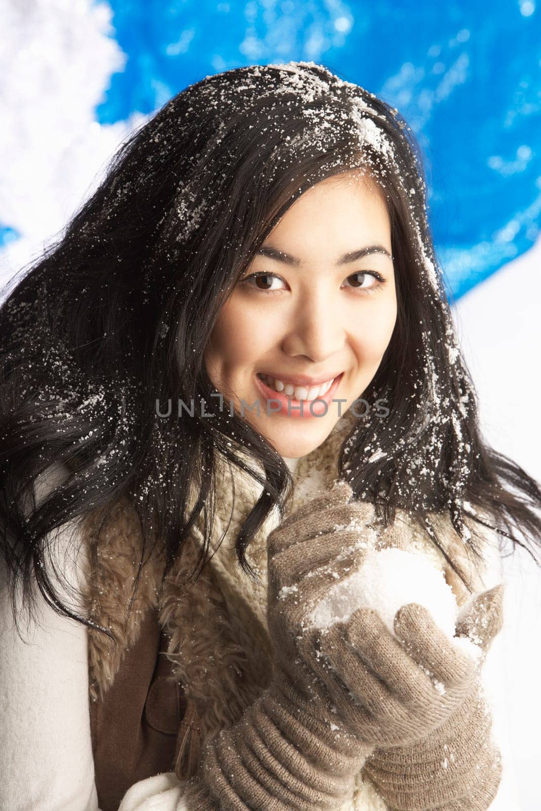 Young Woman Wearing Warm Winter Clothes Holding Snowball In Studio