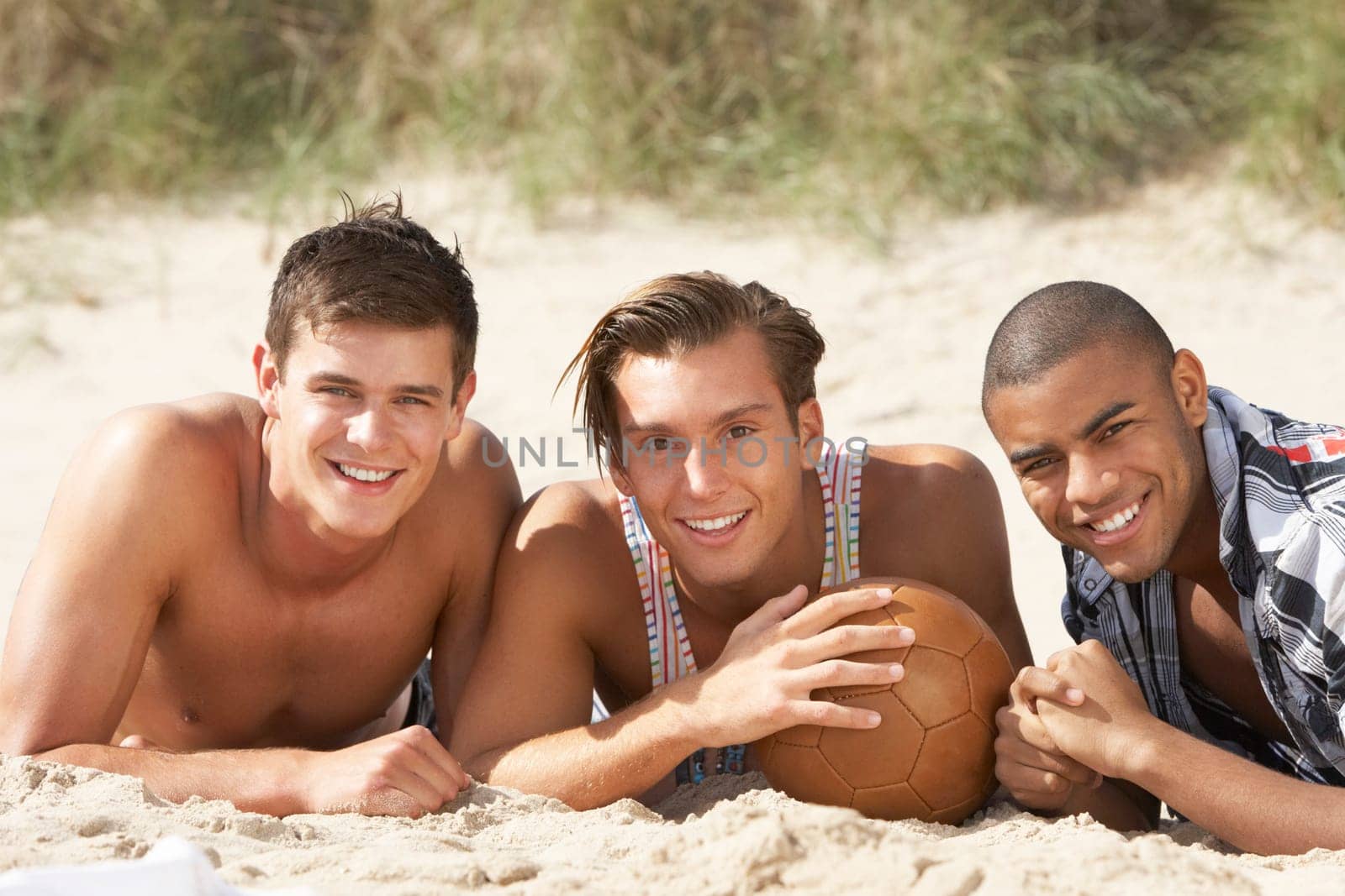 Three Young Men Relaxing On Beach With Football Together