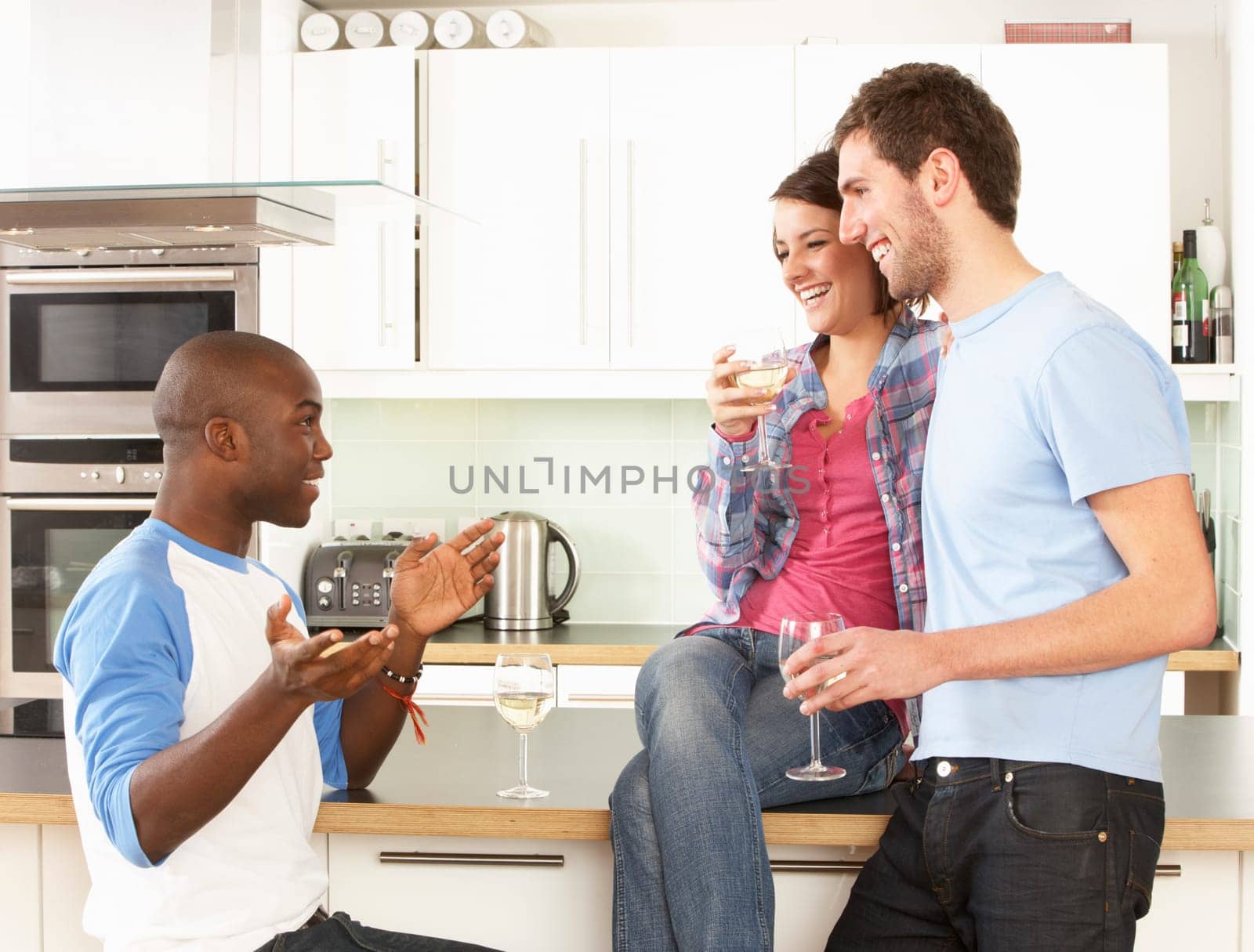 Group Of Young Friends Enjoying Glass Of Wine In Modern Kitchen