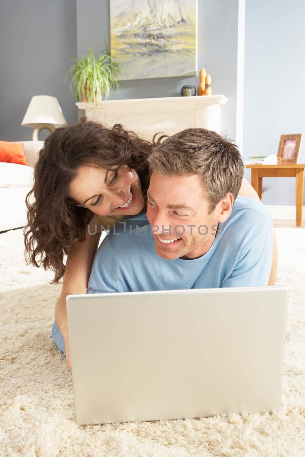 Couple Using Laptop Relaxing Laying On Rug At Home