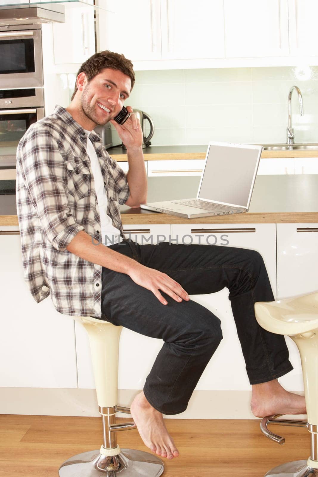 Young Man Relaxing Sitting In Kitchen Talking On Phone
