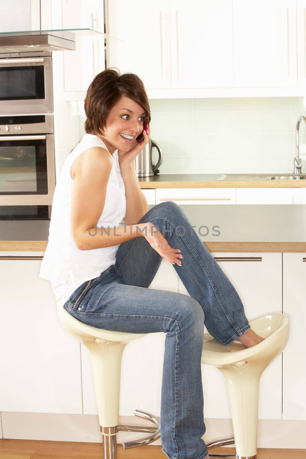 Young Woman Relaxing Sitting In Kitchen Talking On Phone