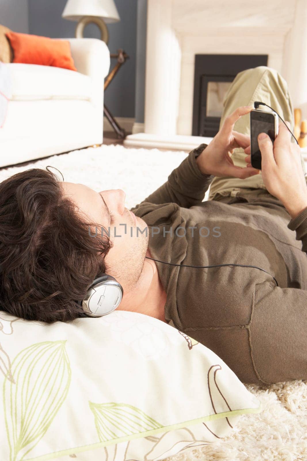Man Listening To MP3 Player On Headphones Relaxing Laying On Rug At Home