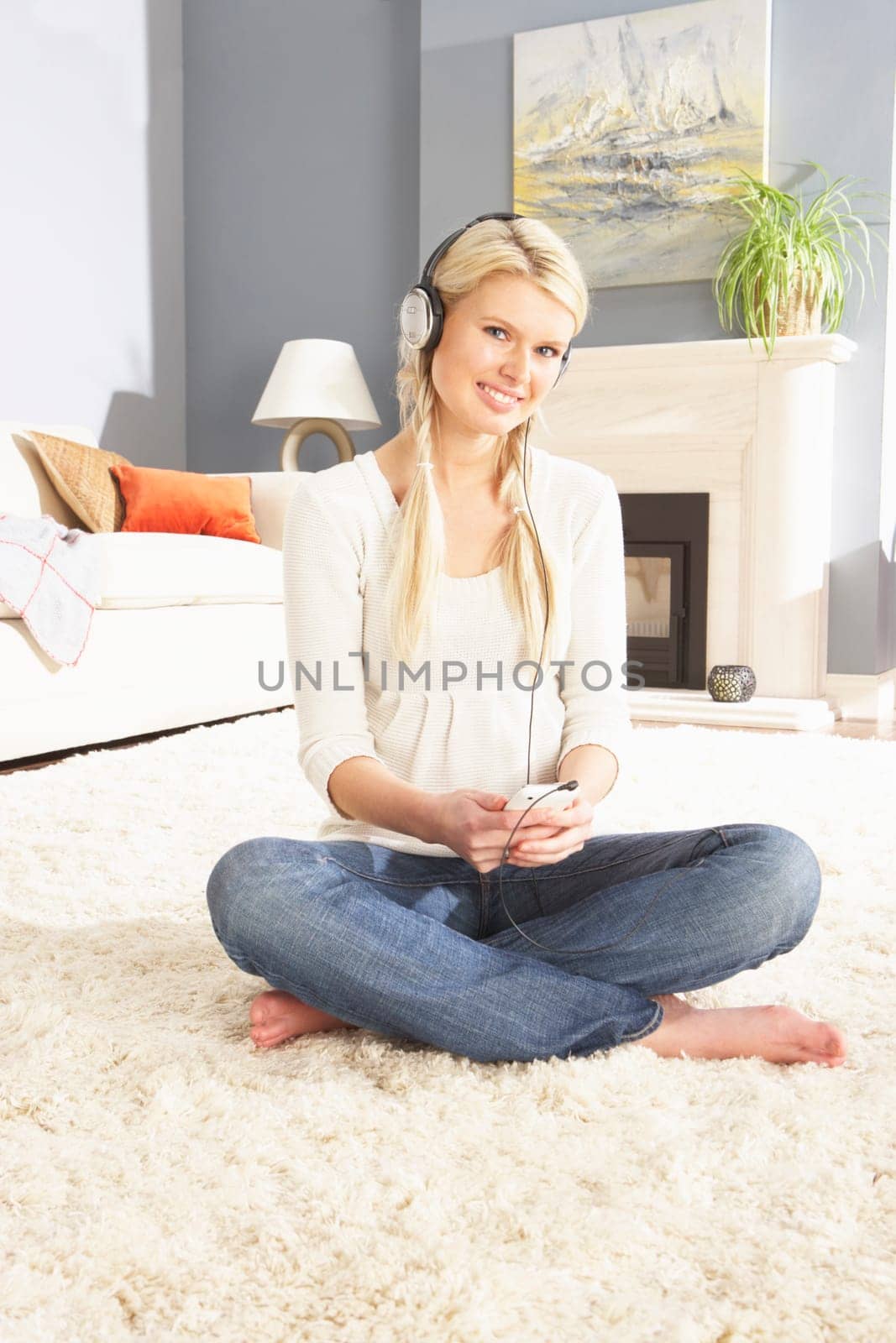 Woman Listening To MP3 Player On Headphones Relaxing Sitting On Rug At Home