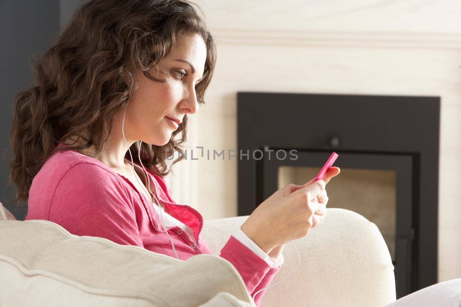 Woman Listening To MP3 Player On Headphones Relaxing Sitting On Rug At Home