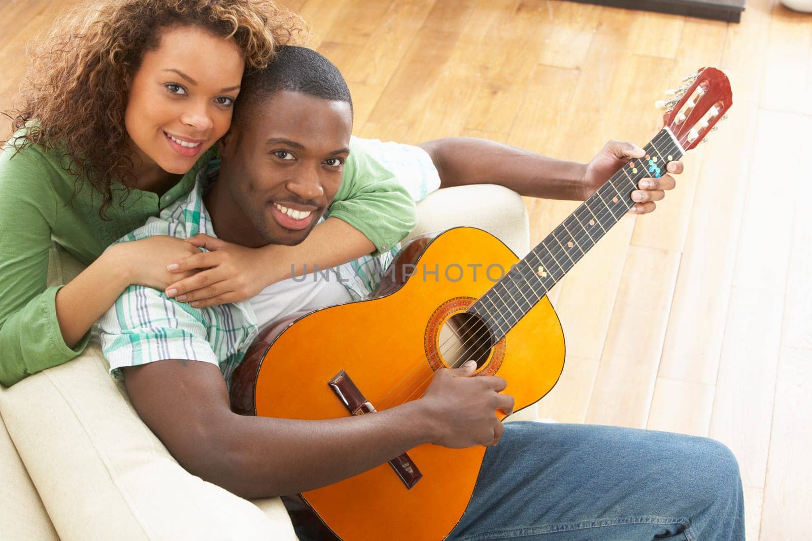 Young Couple Relaxing Sitting On Sofa Playing Acoustic Guitar