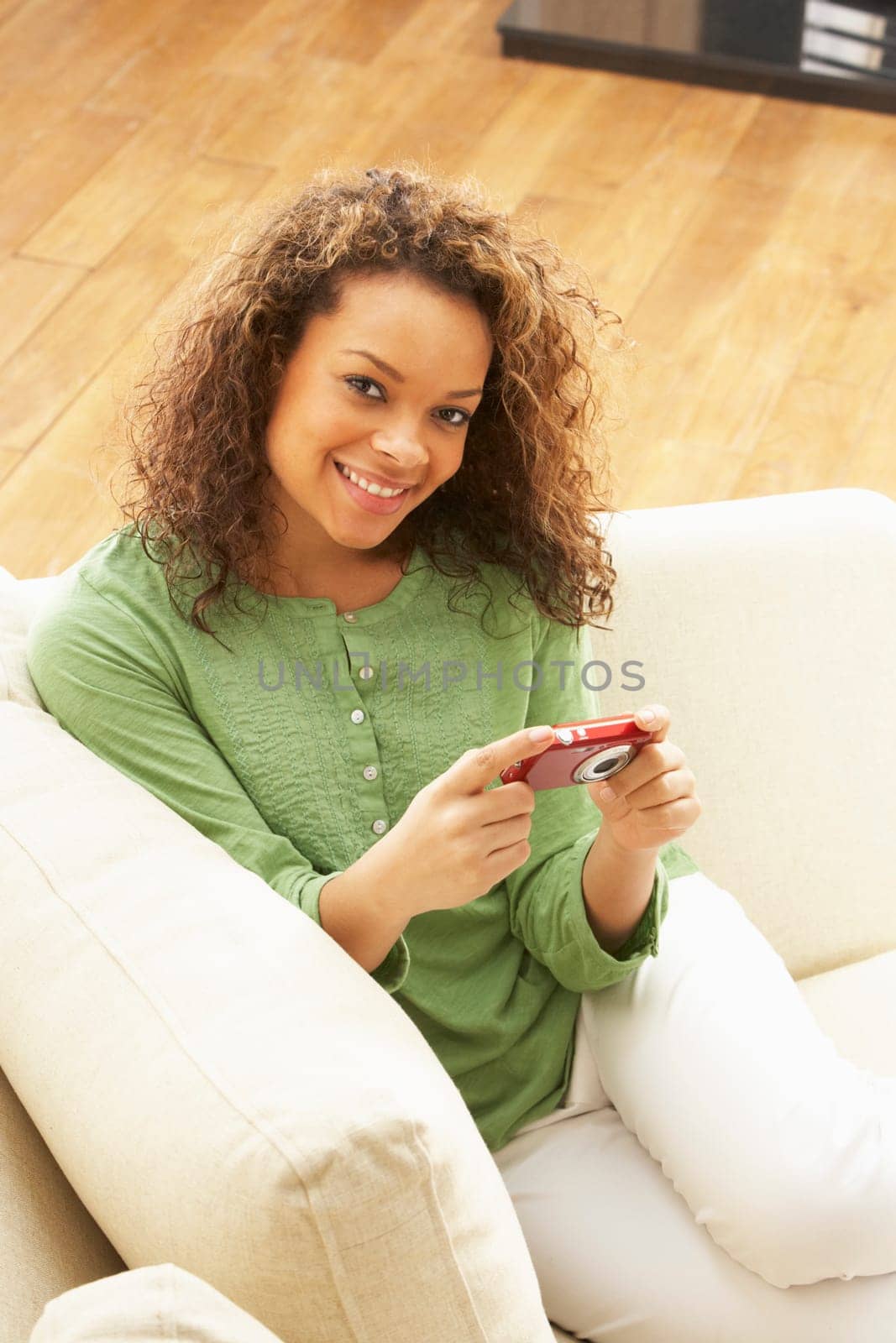 Woman Looking At Pictures On Digital Camera Relaxing Sitting On Sofa At Home