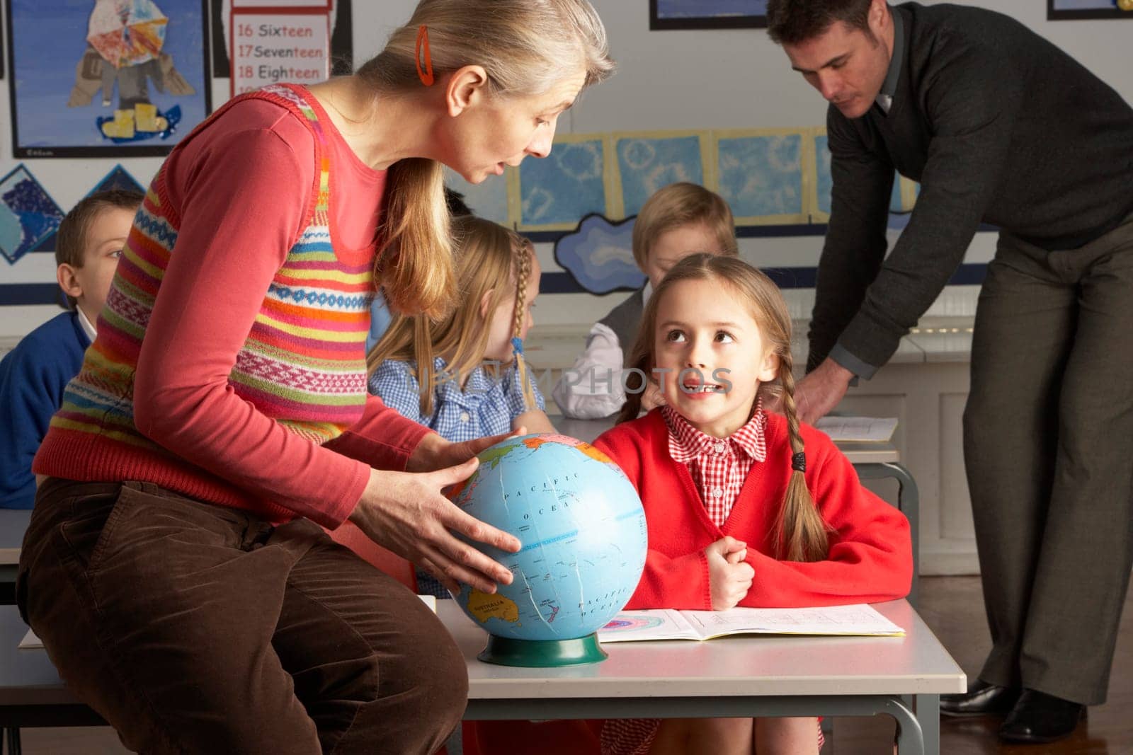 Teachers Giving Geography Lesson To Primary School Children In Classroom