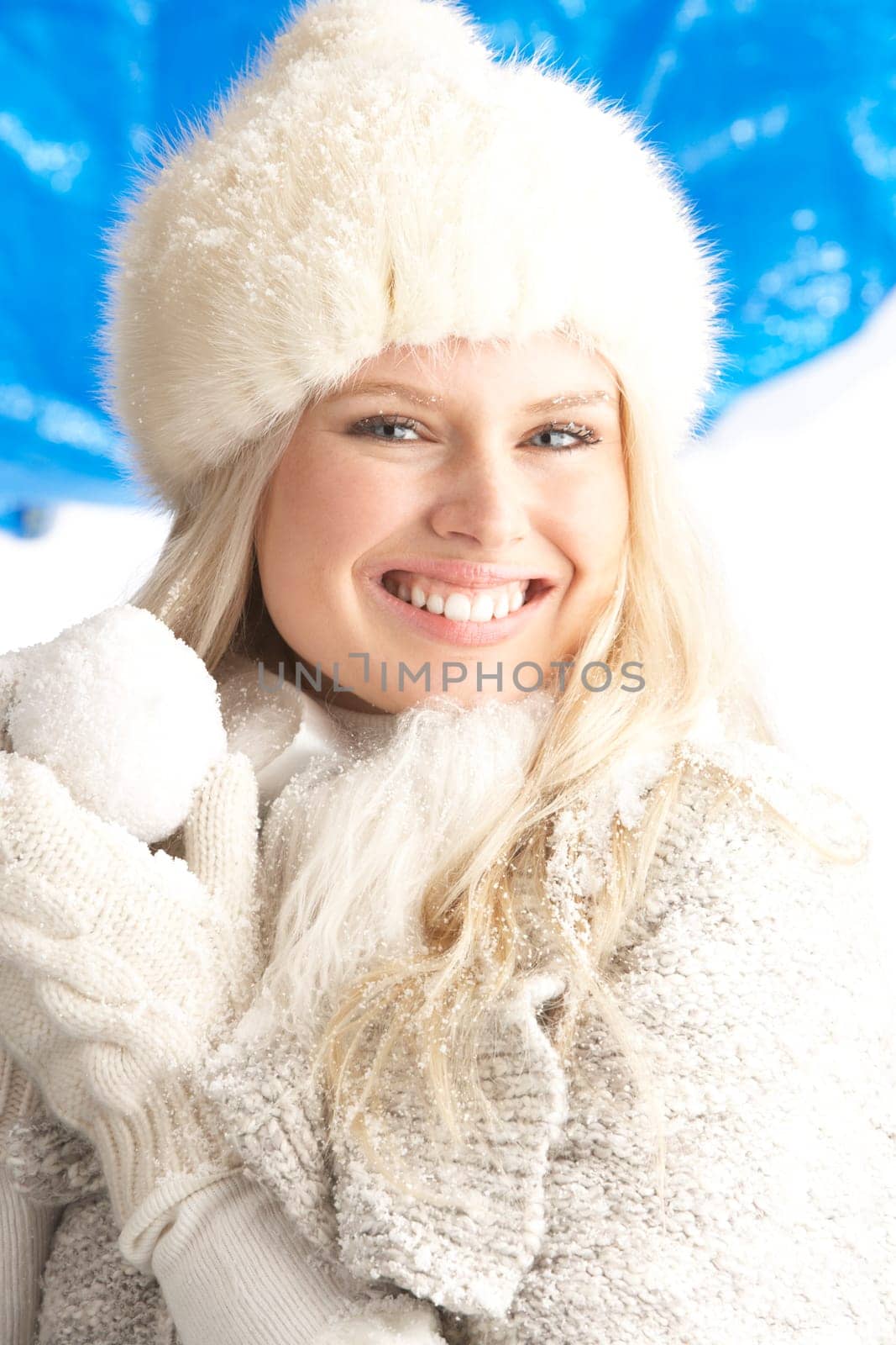 Young Woman Wearing Warm Winter Clothes And Fur Hat Holding Snowball In Studio