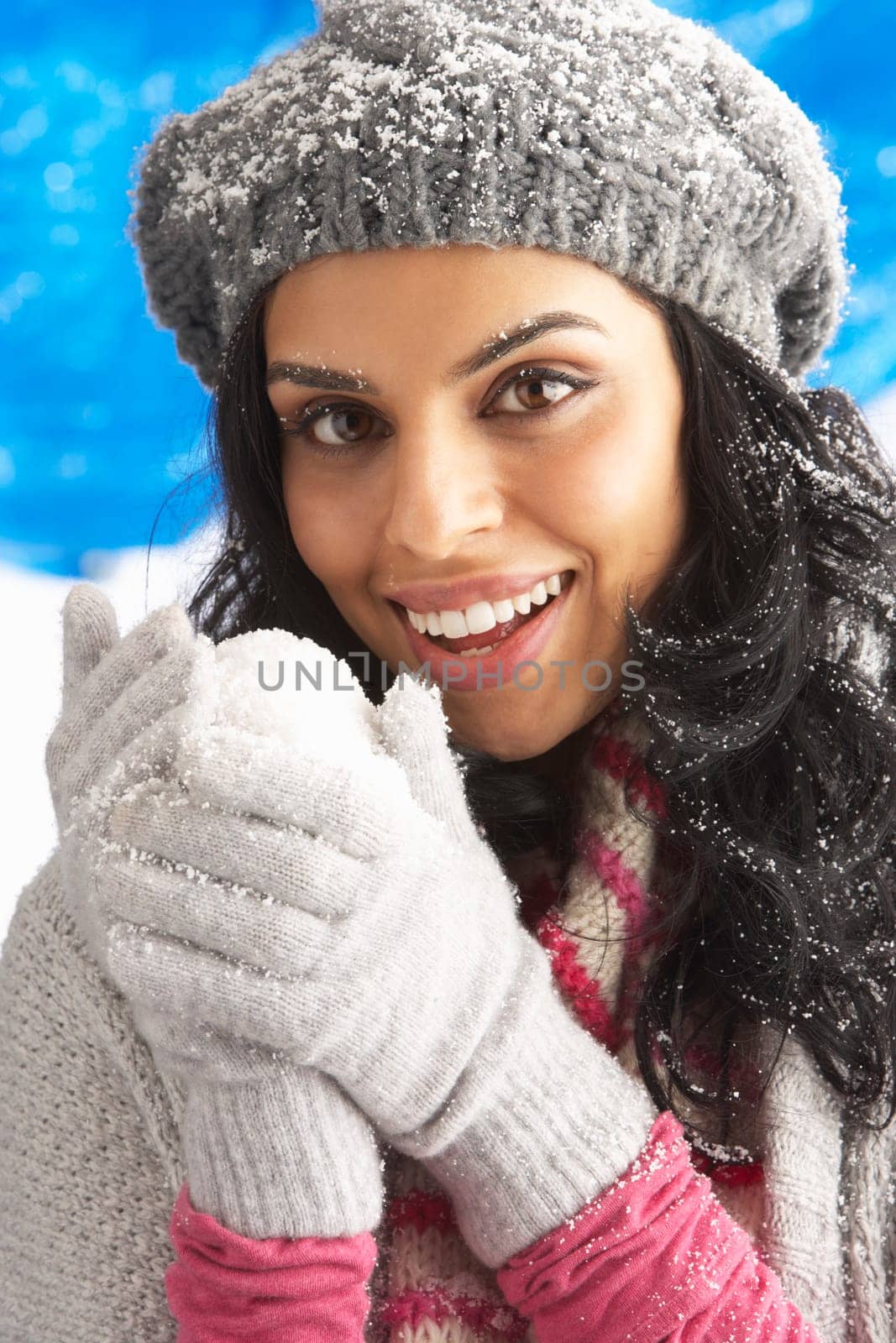 Young Woman Wearing Warm Winter Clothes And Hat Holding Snowball In Studio