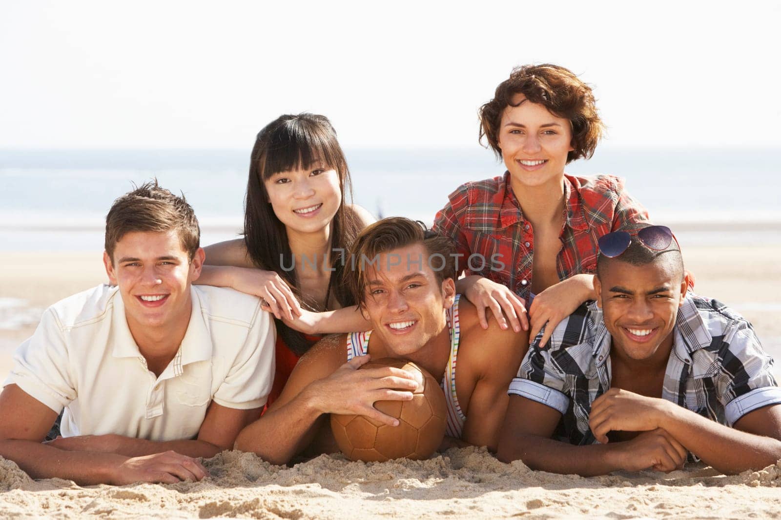 Group Of Friends Relaxing On Beach With Football Together