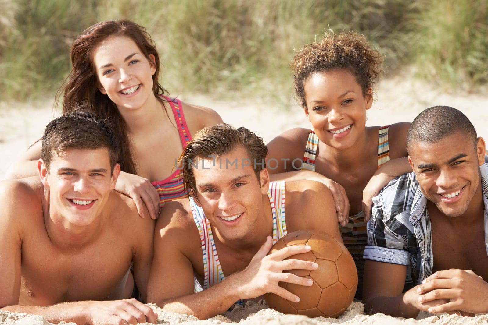 Group Of Friends Relaxing On Beach With Football Together