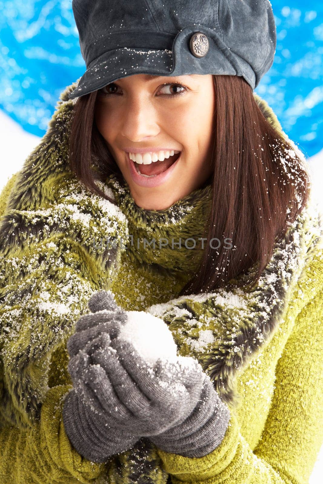 Young Woman Wearing Warm Winter Clothes And Hat Holding Snowball In Studio