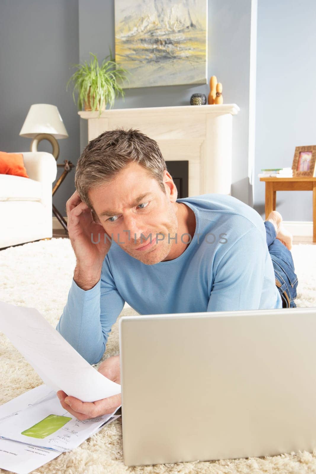 Man Using Laptop To Manage Household Bills Laying On Rug At Home