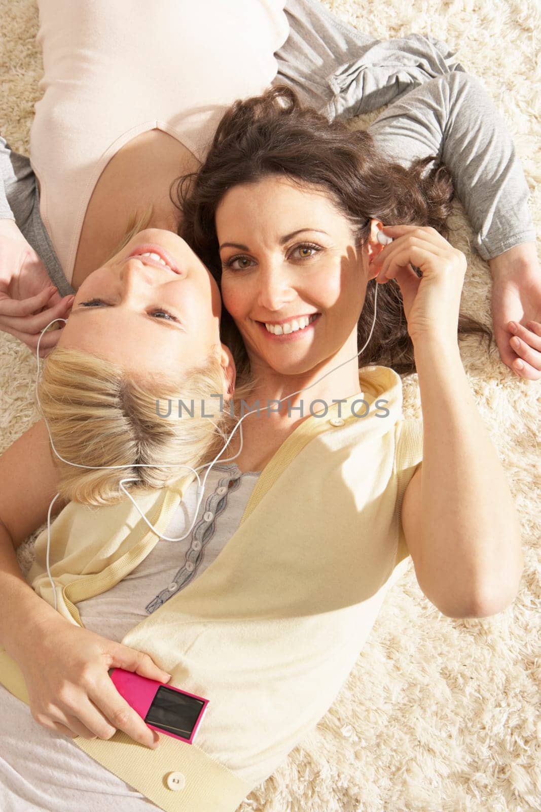 Two Women Listening To MP3 Player On Headphones Together Relaxing Laying On Rug At Home
