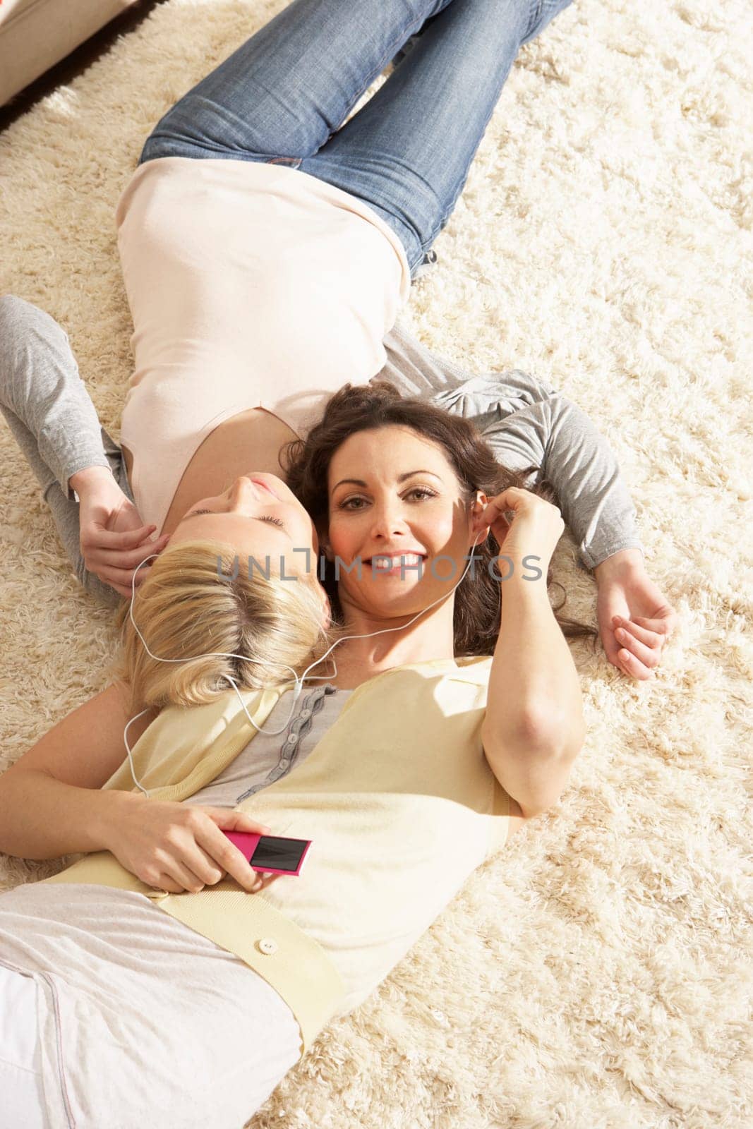 Two Women Listening To MP3 Player On Headphones Together Relaxing Laying On Rug At Home