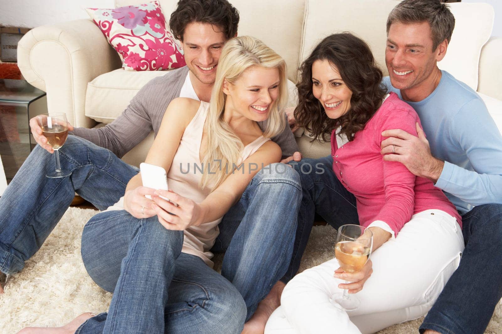 Group Of Friends Looking At Pictures On Smartphone At Home