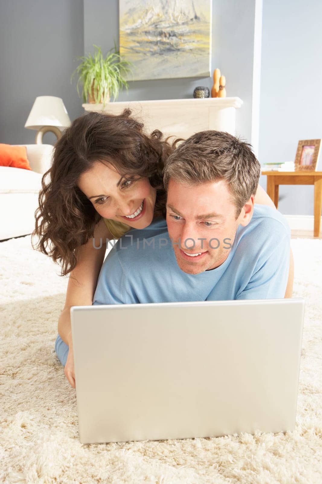 Couple Using Laptop Relaxing Laying On Rug At Home