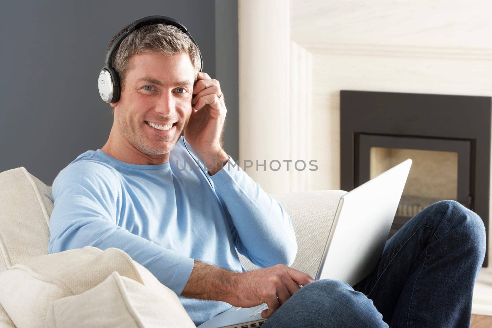 Man Using Laptop Wearing Headphones Relaxing Sitting On Sofa At Home