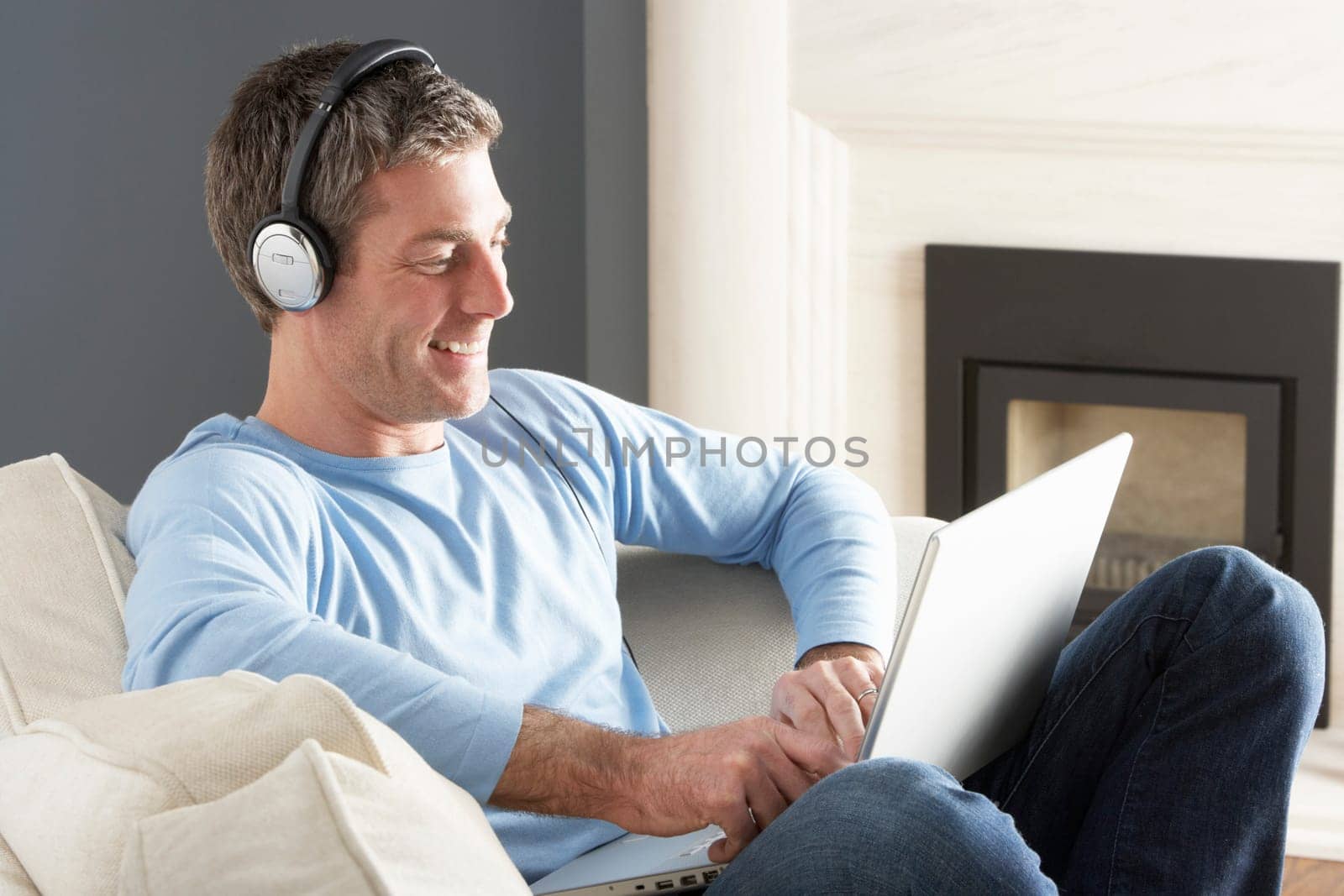 Man Using Laptop Wearing Headphones Relaxing Sitting On Sofa At Home