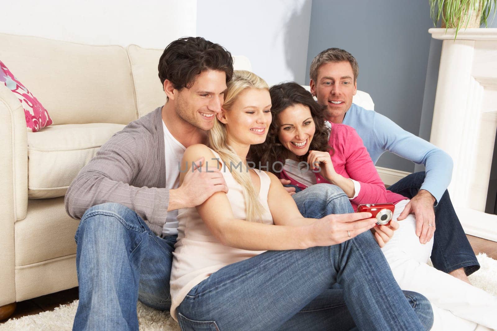 Group Of Friends Looking At Pictures On Digital Camera At Home