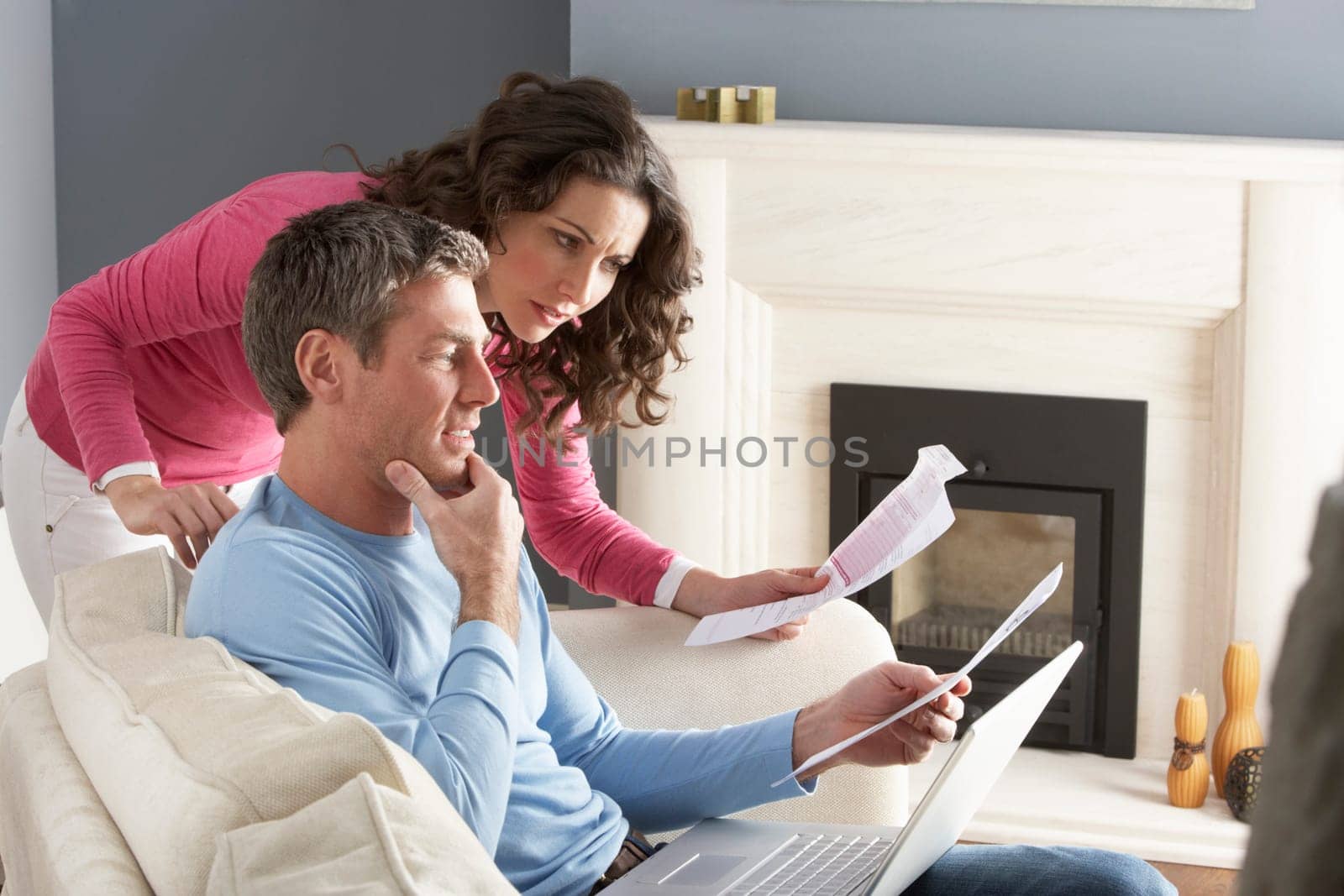 Couple Using Laptop And Discussing Household Bills Sitting On Sofa At Home