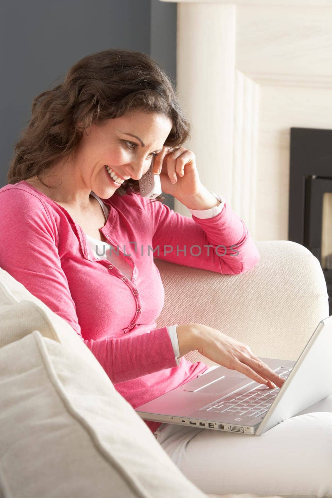 Woman Using Laptop Relaxing Sitting On Sofa At Home Talking On Phone
