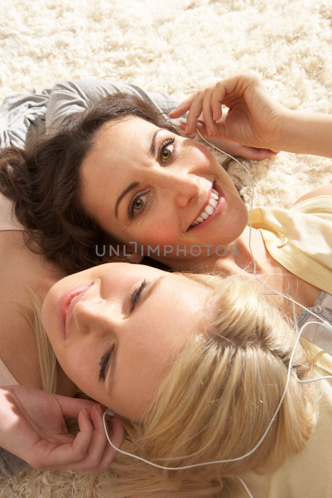 Two Women Listening To MP3 Player On Headphones Together Relaxing Laying On Rug At Home
