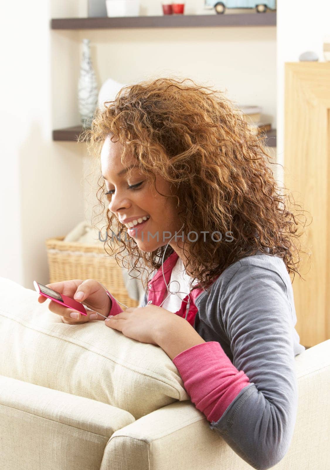 Woman Listening To MP3 Player On Headphones Relaxing Sitting On Rug At Home