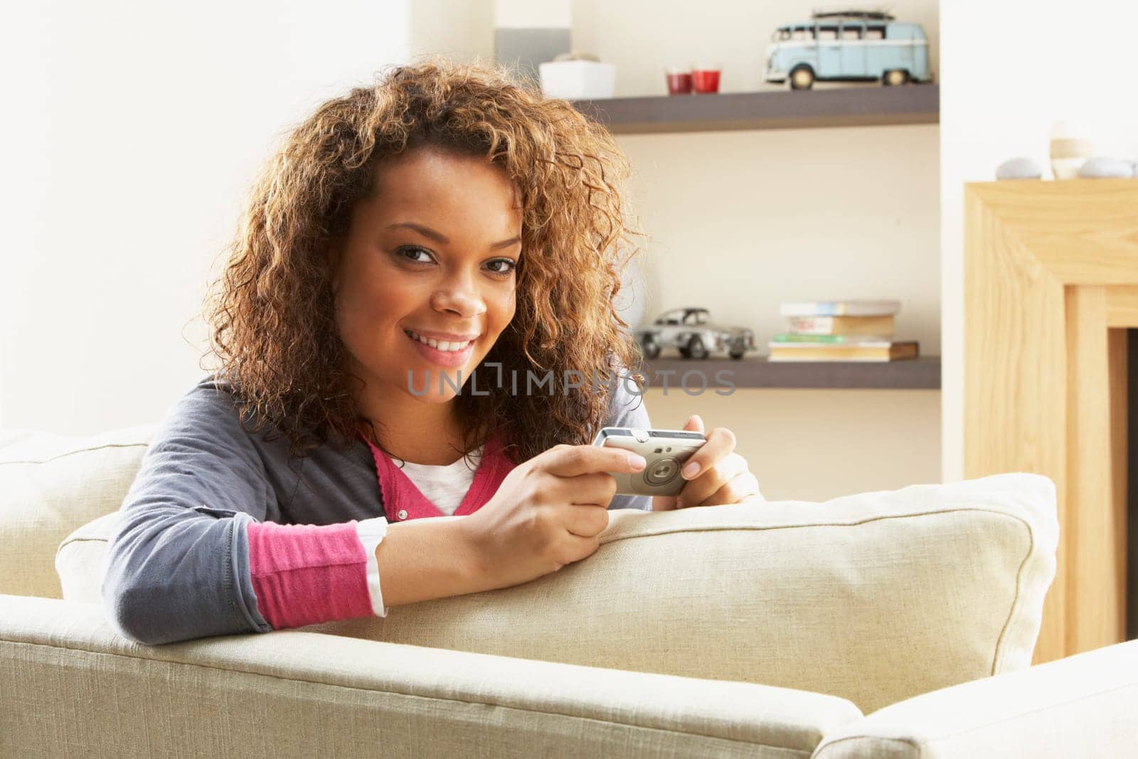 Woman Looking At Pictures On Digital Camera Relaxing Sitting On Sofa At Home
