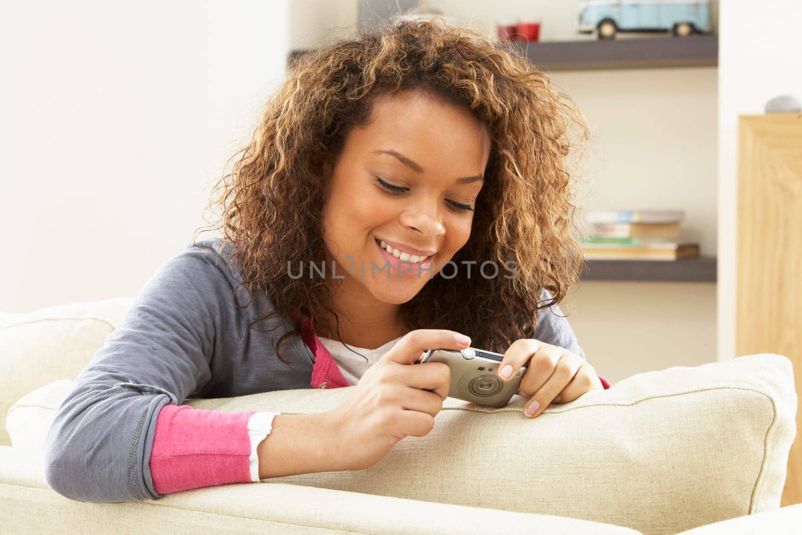 Woman Looking At Pictures On Digital Camera Relaxing Sitting On Sofa At Home