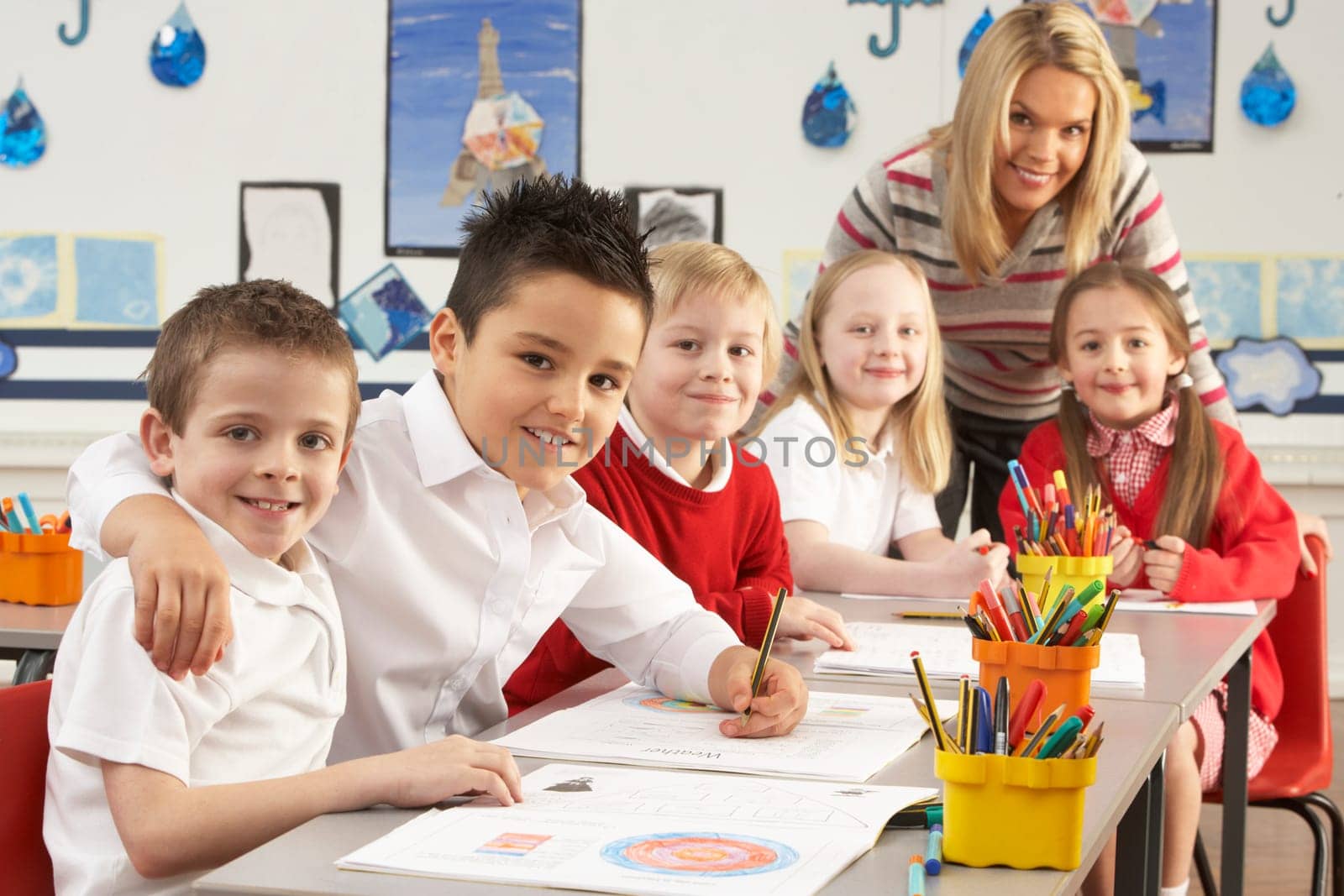 Group Of Primary Schoolchildren And Teacher Working At Desks In Classroom