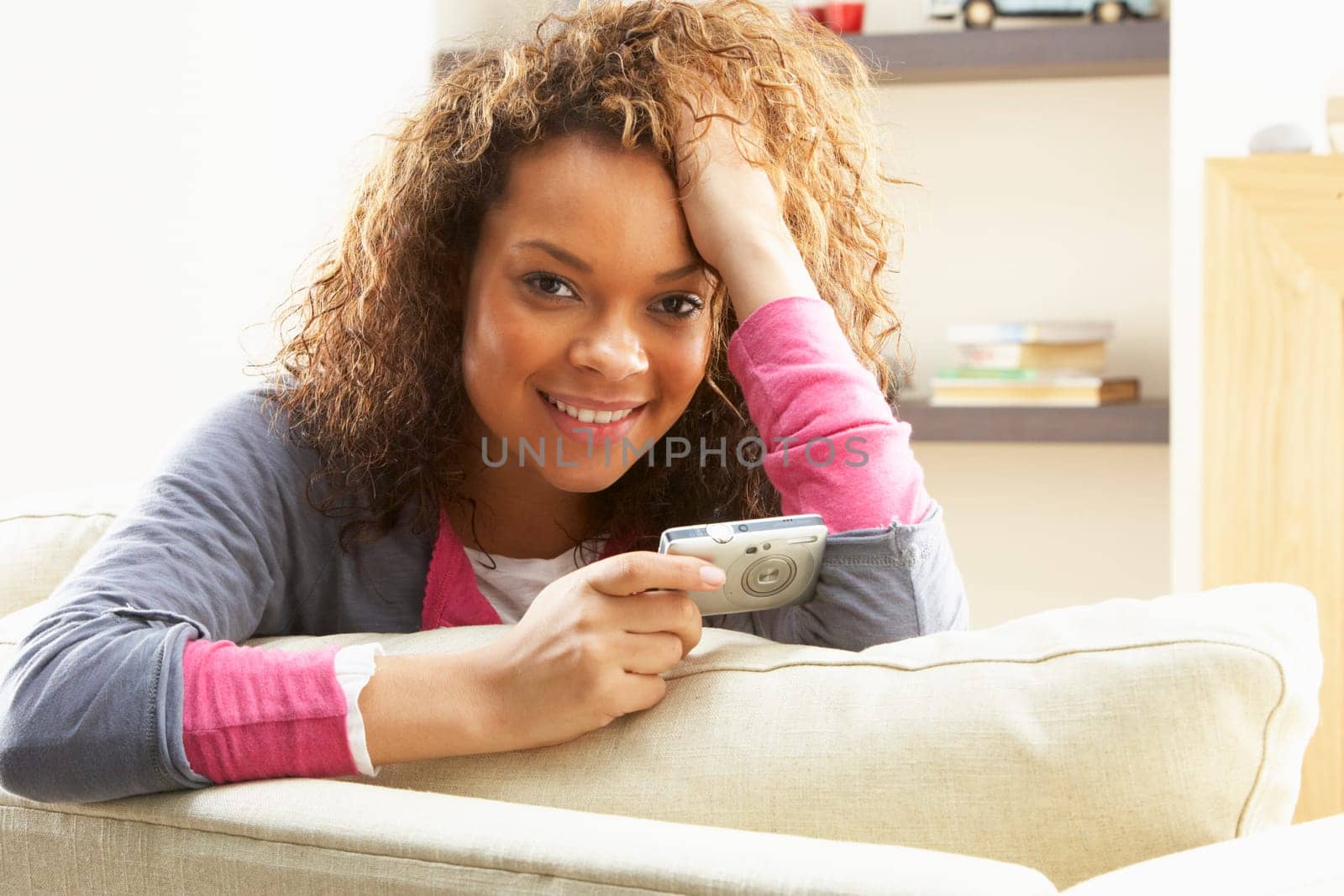 Woman Looking At Pictures On Digital Camera Relaxing Sitting On Sofa At Home