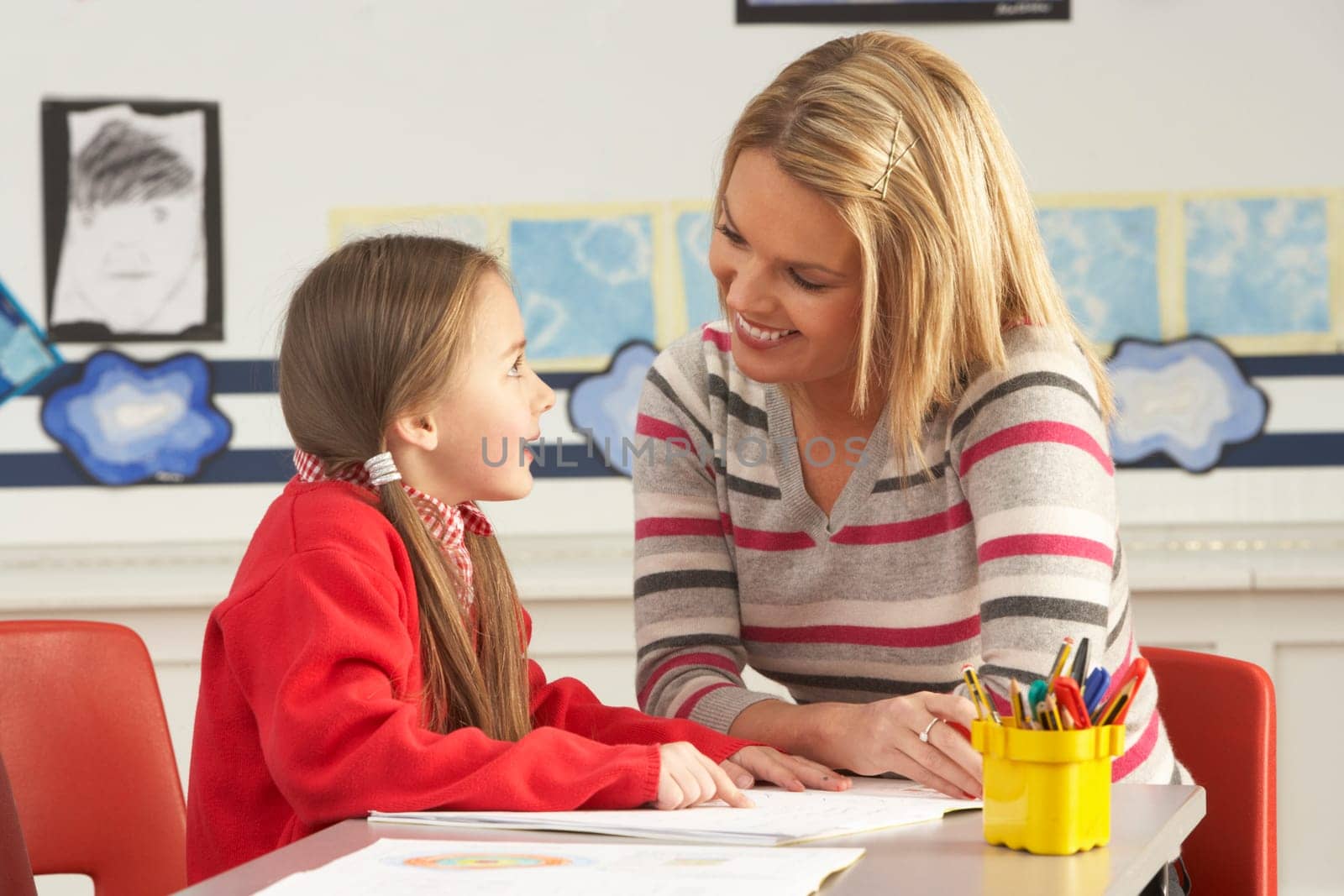 Female Primary School Pupil And Teacher Working At Desk In Classroom
