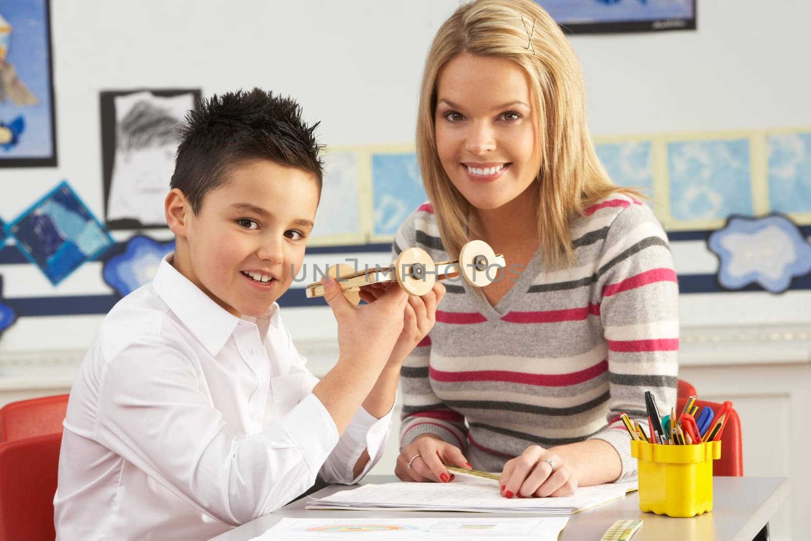 Male Primary School Pupil And Teacher Working At Desk In Classroom