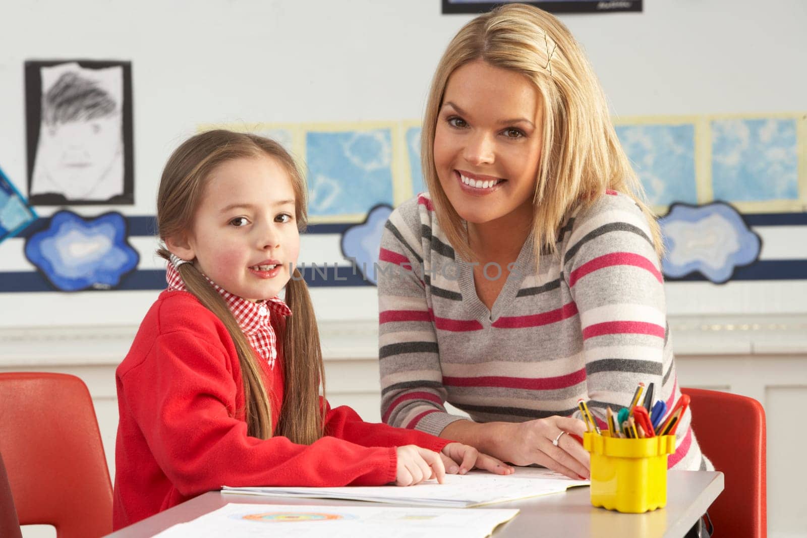 Female Primary School Pupil And Teacher Working At Desk In Classroom