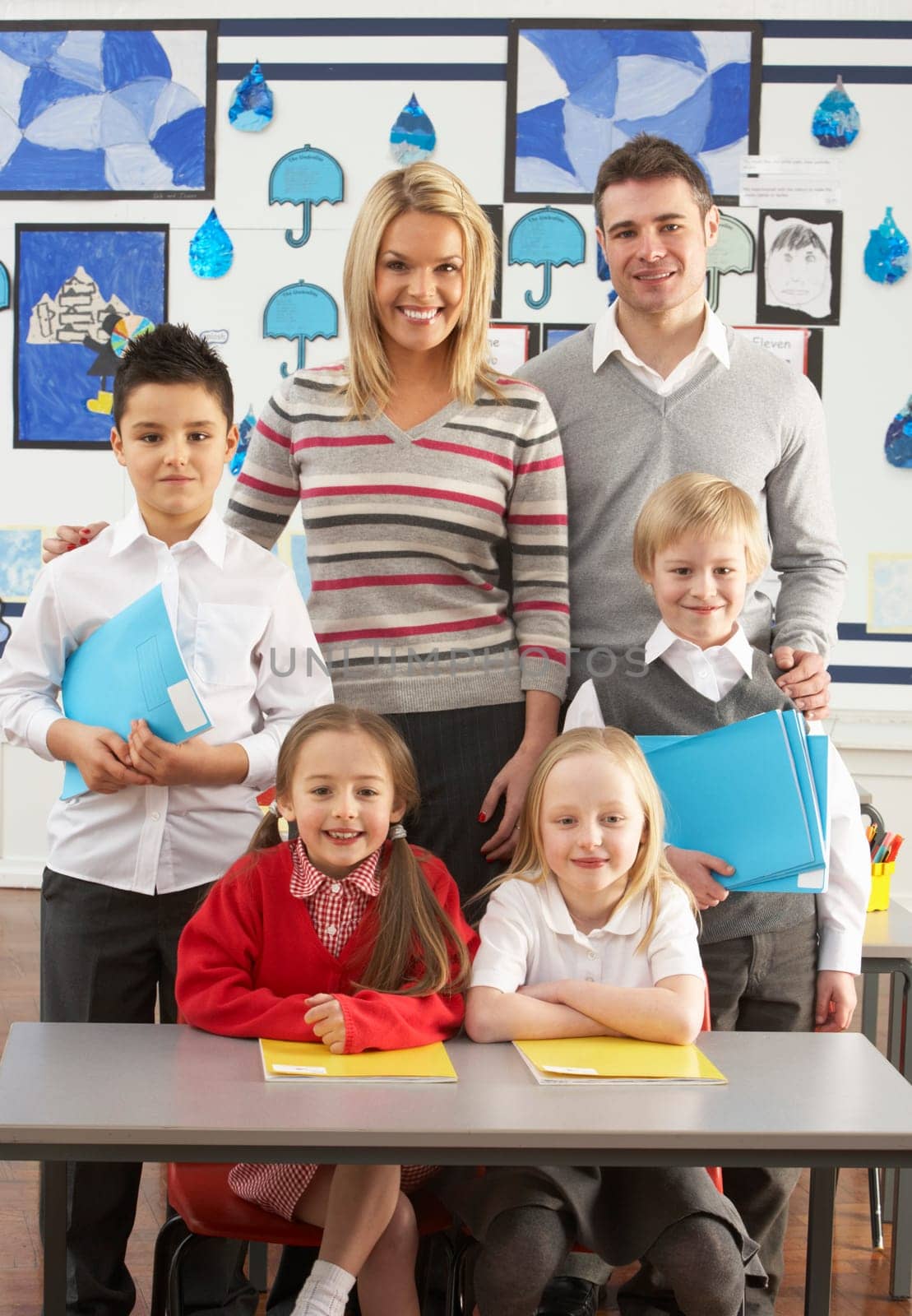Portrait Of Group Of Primary Schoolchildren And Teachers Sitting At Desk In Classroom