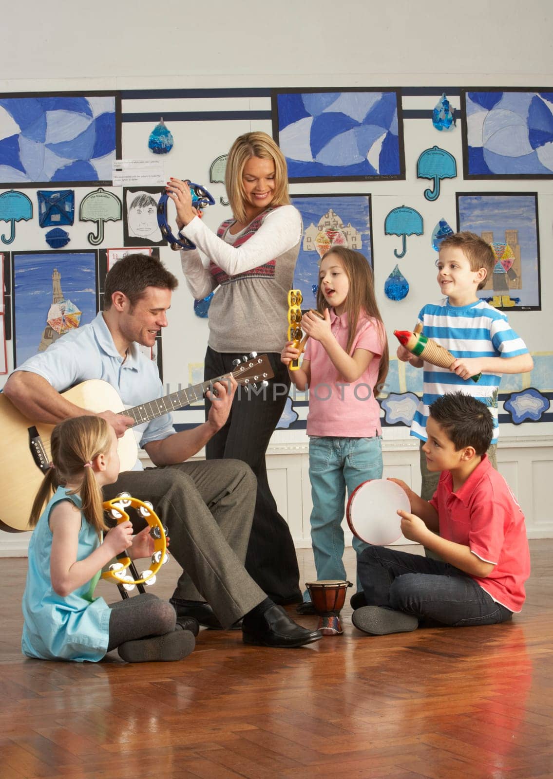 Teachers Playing Guitar With Pupils Having Music Lesson In Classroom