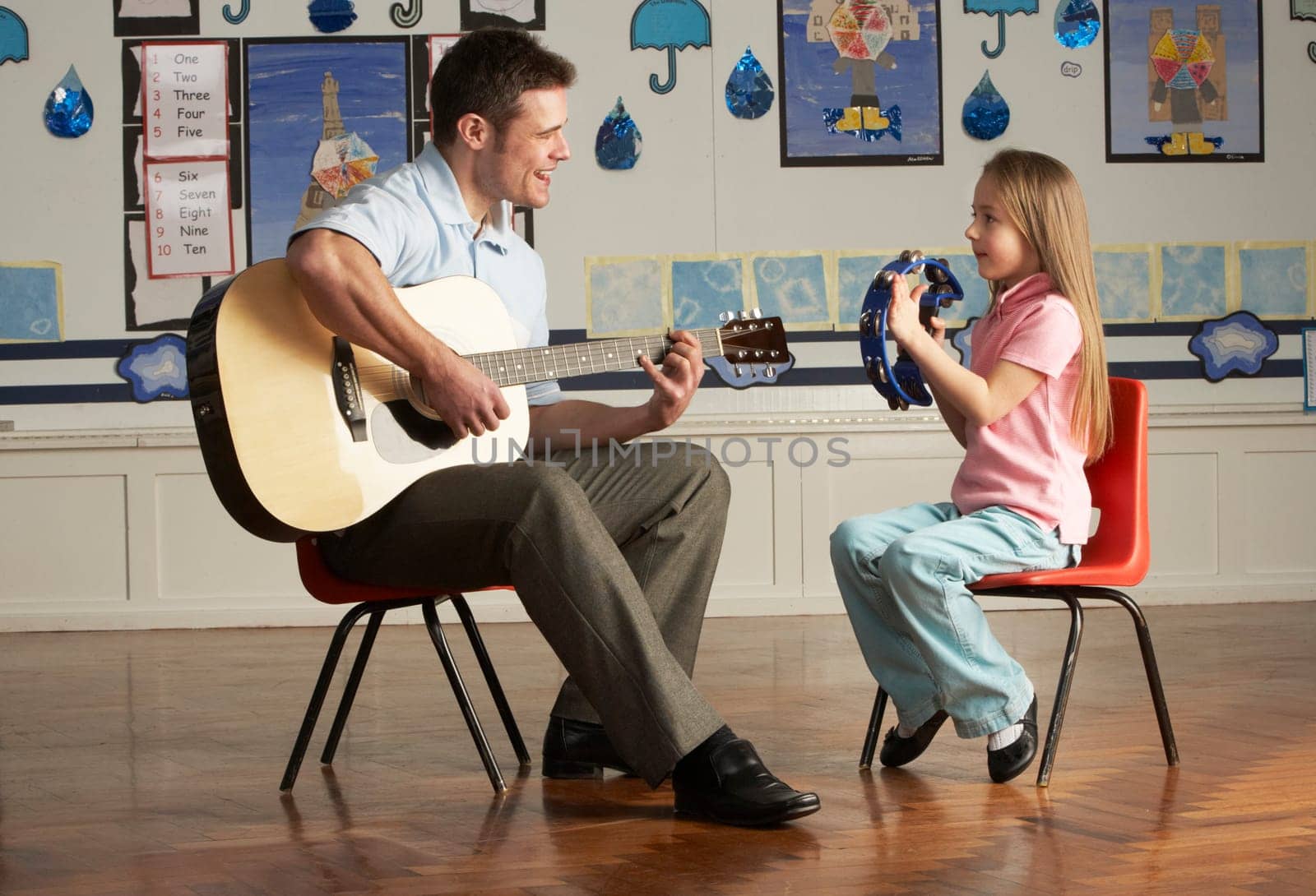 Male Teacher Playing Guitar With Pupil In Classroom