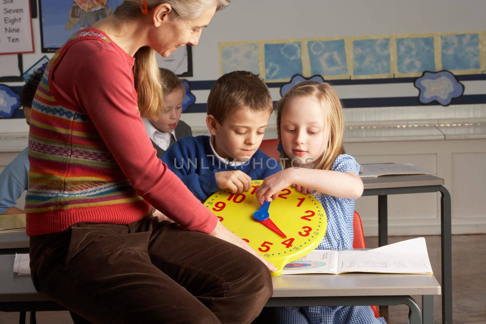 Female Teacher In Primary School Teaching Children To Tell Time In Classroom