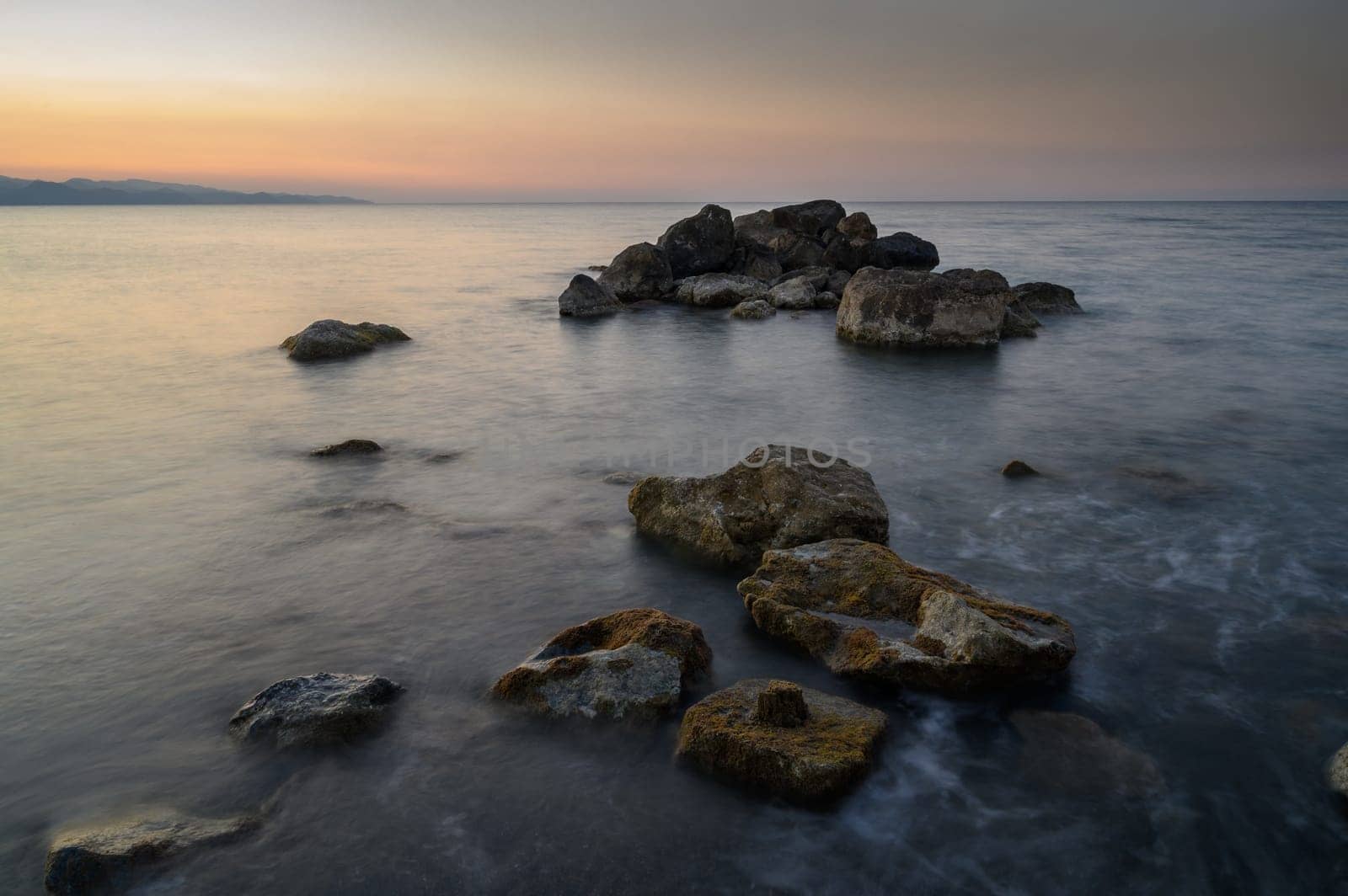 Gentle waves lap against smooth stones as twilight casts a tranquil glow over the peaceful shoreline.