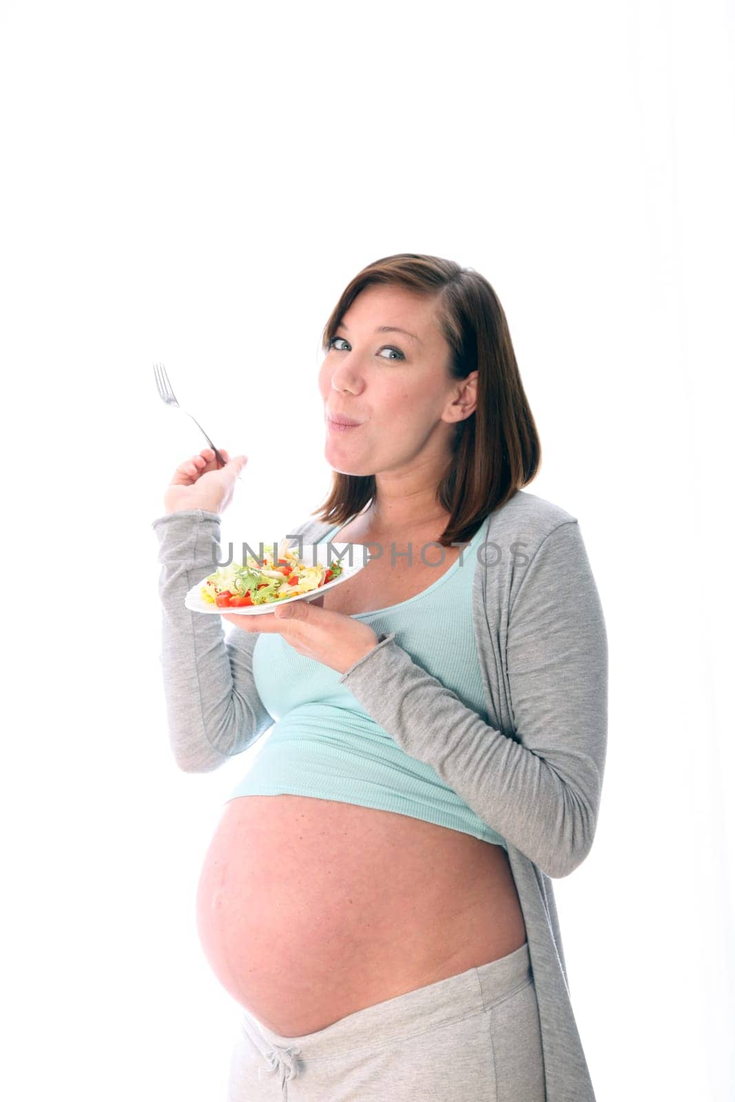 Pregnant woman eating healthy salad. She holds a plate and fork in her hand and enjoys her healthy food