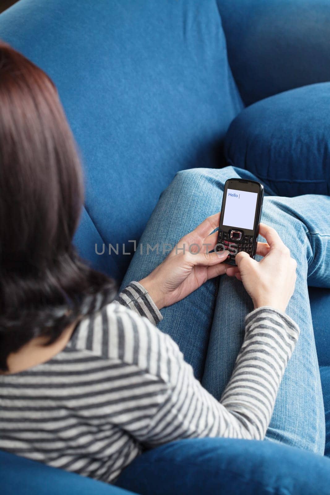 Young brunette woman sitting on blue sofa and texting with her cellphone