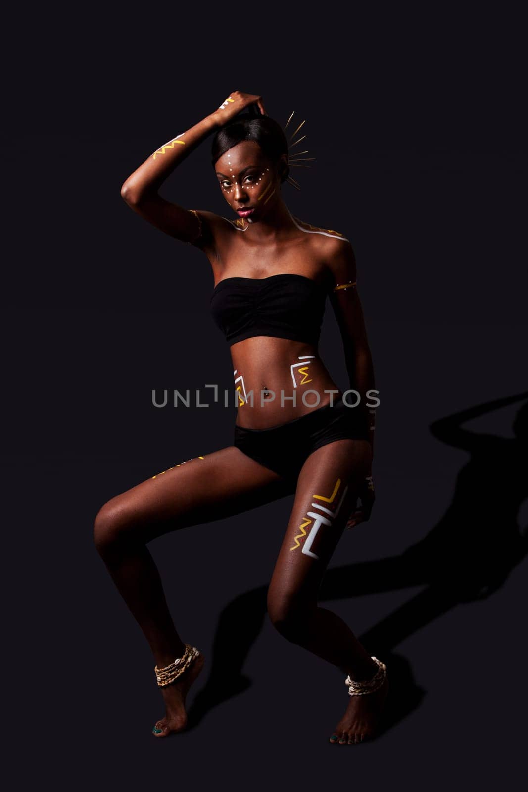 Beautiful exotic African female fashion with tribal yellow red and white cultural makeup cosmetics and sticks in hair, in cultural dance position.