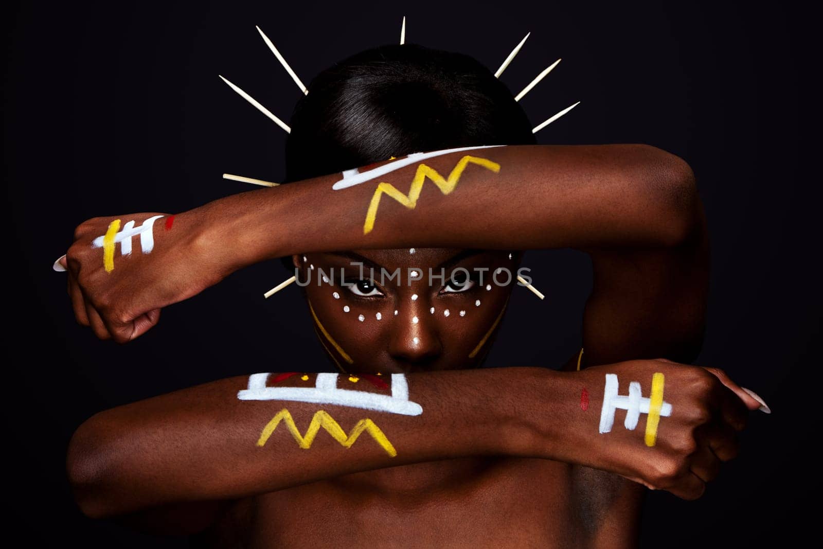 Beautiful cultural tribal African female face with arms and hands in fron, yellow, red and white makeup cosmetics lines dots, sticks in hair.