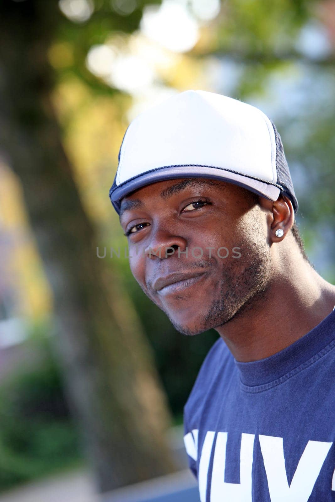 A smiling young African-American looks towards the camera. He wears a white cap.