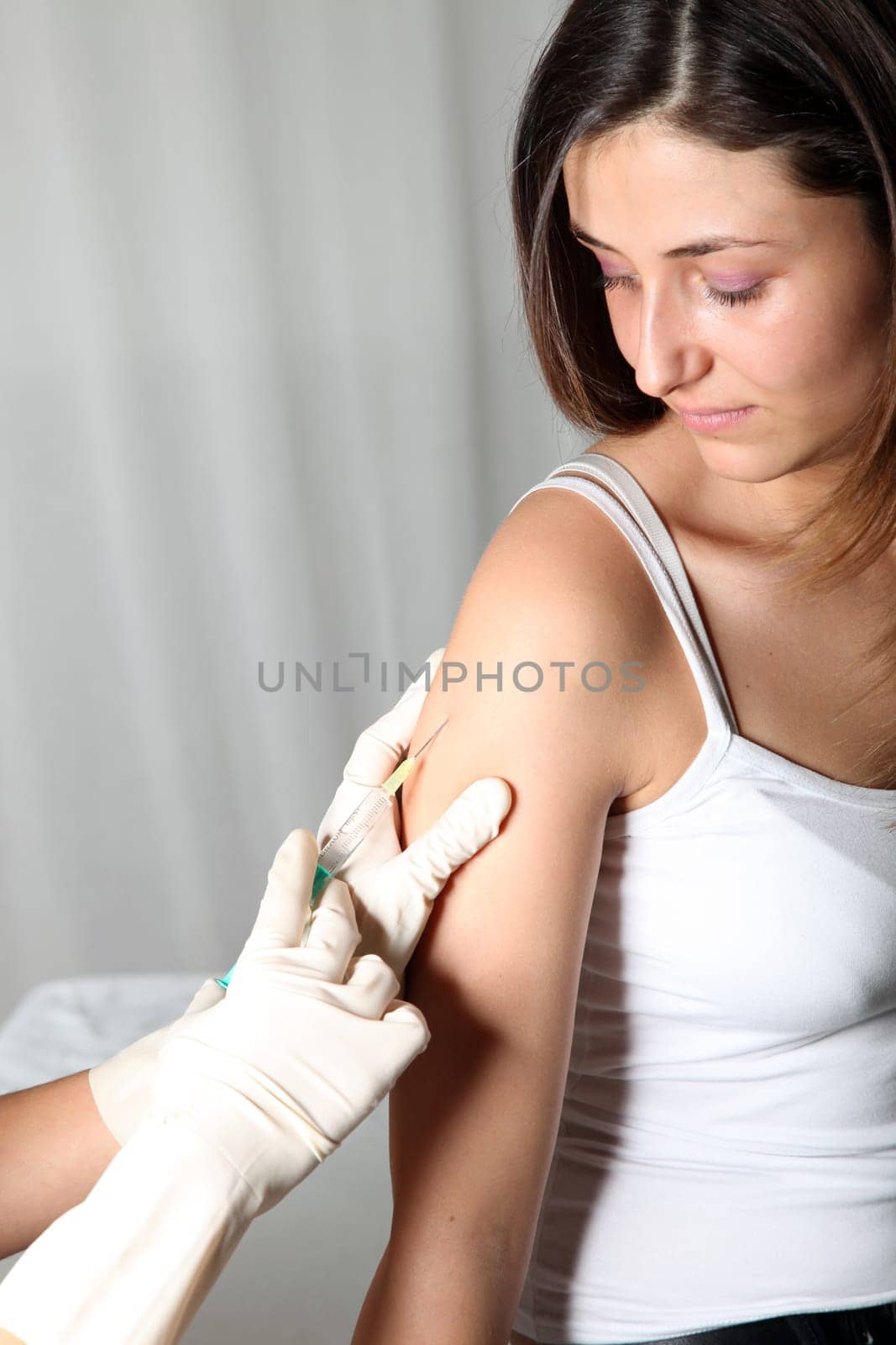 Young woman receives an injection at doctor. She receives the injection into the upper arm
