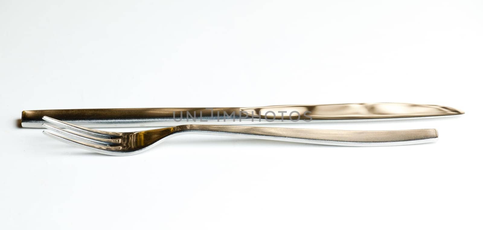 Knive and fork from modern stainless steel design isolated against white and reflecting brown golden light