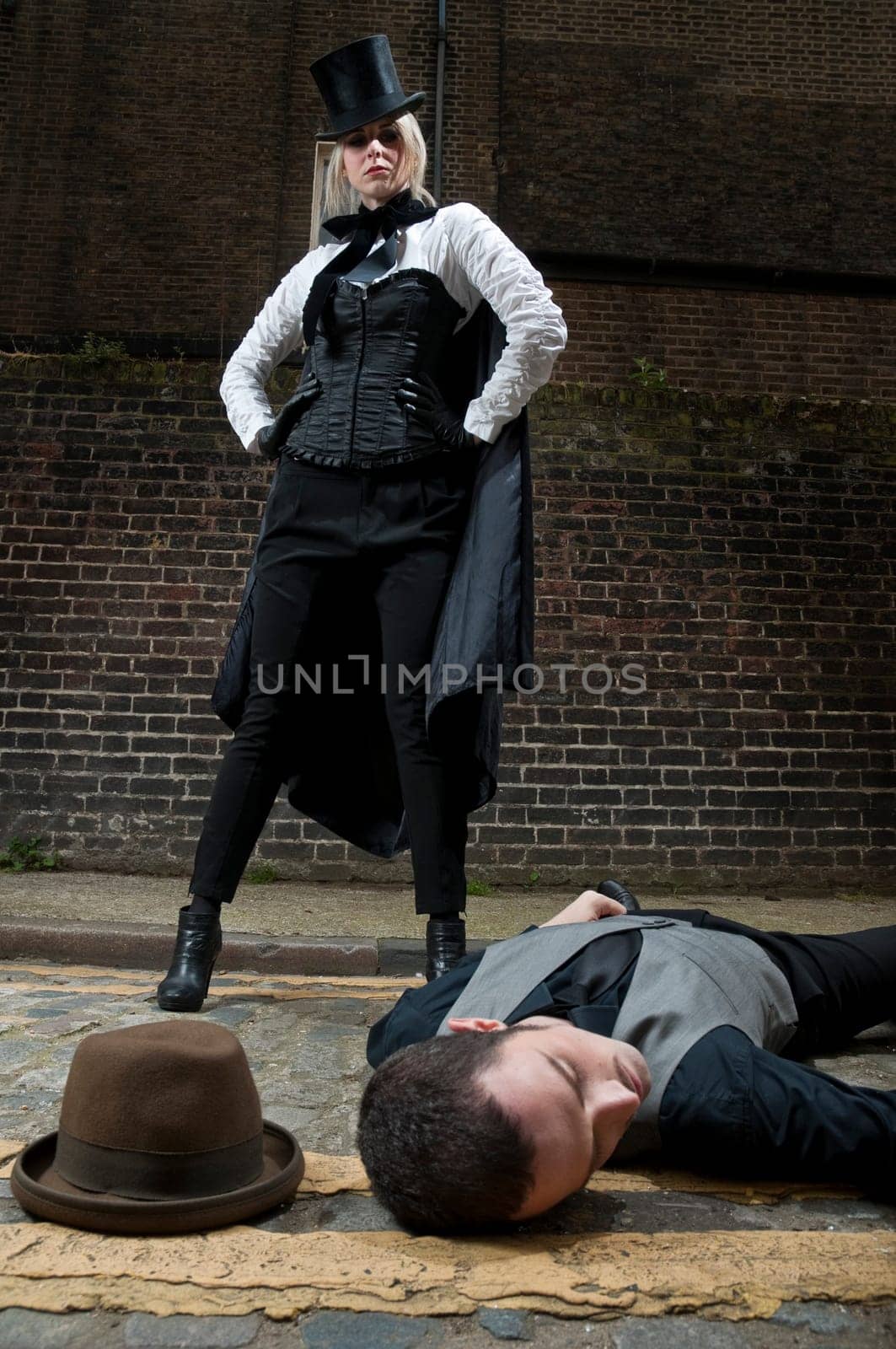 Woman dressed as Jack the Ripper on top of man lying on the ground.